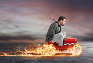 man sitting on a tiny go-cart with the wheels in flames leaving a trail of fire