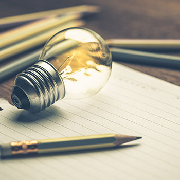 Lit lightbulb and pencil on top of lined paper with several pencils blurred behind